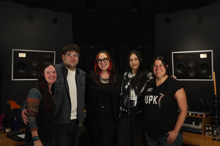 Members of the RISER collective posing together inside a music recording studio with wall-mounted studio monitors in the background.